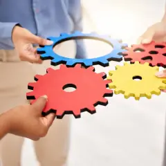 Ludzie łączą kolorowe trybiki, symbolizując współpracę i persfazję w osiąganiu wspólnego celu.