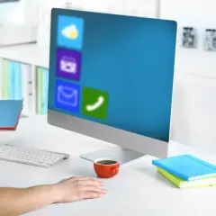 Pracownik biurowy z notatnikiem w dłoni, przed monitorem z ikonami aplikacji, jak w WPS Office.