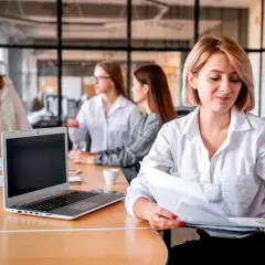 Kobiety w biurze pracują nad projektem. Jedna z nich, blondynka, przegląda dokumenty. To idealna templatka do wizualizacji pracy zespołowej.