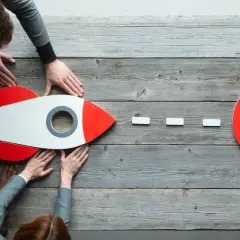 Zespół wspiera rakietę, symbolizującą cel. Właściwa ewaluacja projektu jest kluczem do sukcesu.