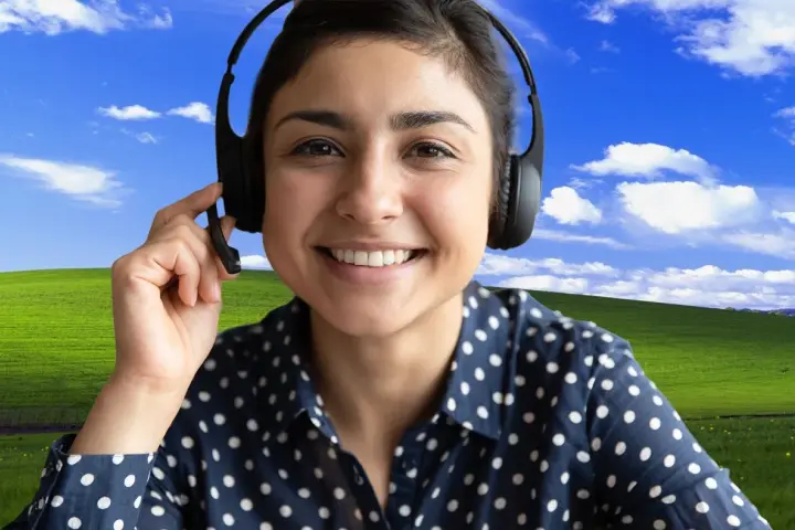 Uśmiechnięta kobieta w słuchawkach z mikrofonem, z klasycznym tłem "Bliss" z Windows XP. Dowiedz się, jak ustawić tło w Teams, by Twoje rozmowy były przyjemniejsze!
