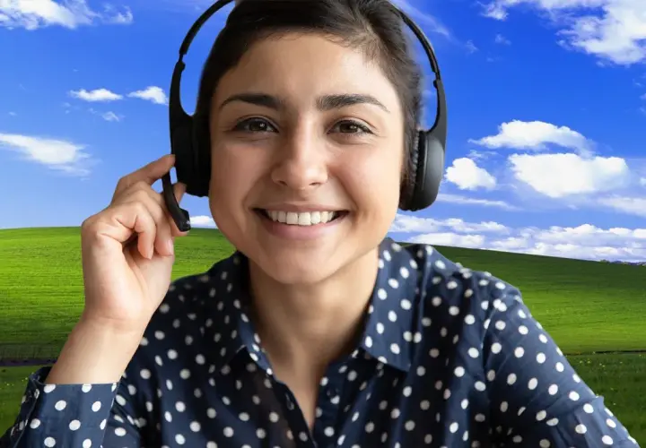 Uśmiechnięta kobieta w słuchawkach z mikrofonem, z klasycznym tłem "Bliss" z Windows XP. Dowiedz się, jak ustawić tło w Teams, by Twoje rozmowy były przyjemniejsze!