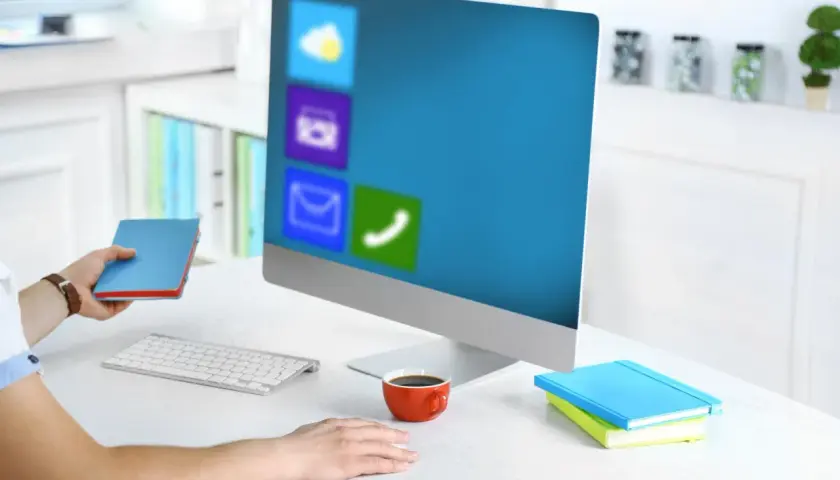 Pracownik biurowy z notatnikiem w dłoni, przed monitorem z ikonami aplikacji, jak w WPS Office.